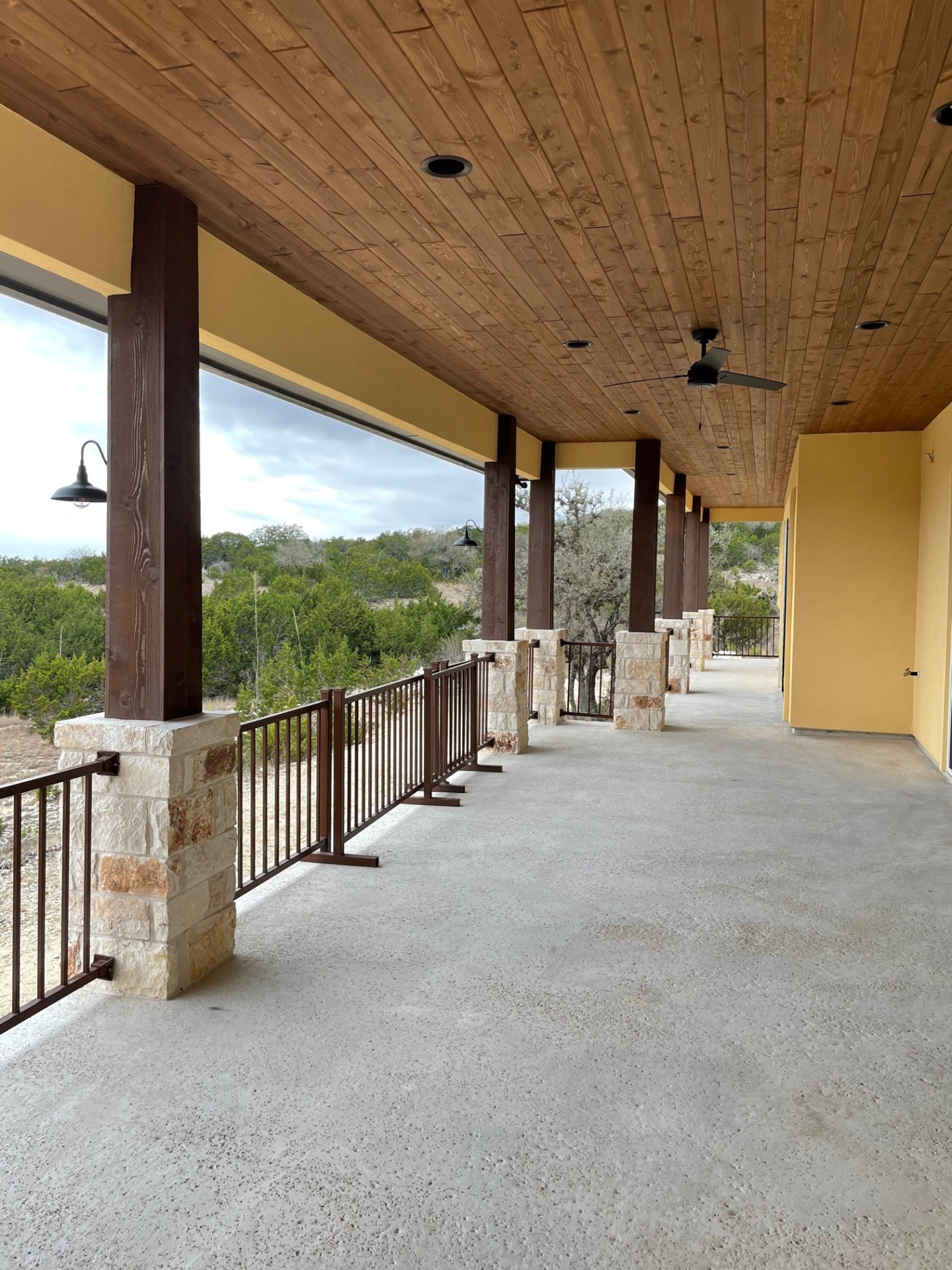 Covered porch with a stained wood ceiling and stone columns
