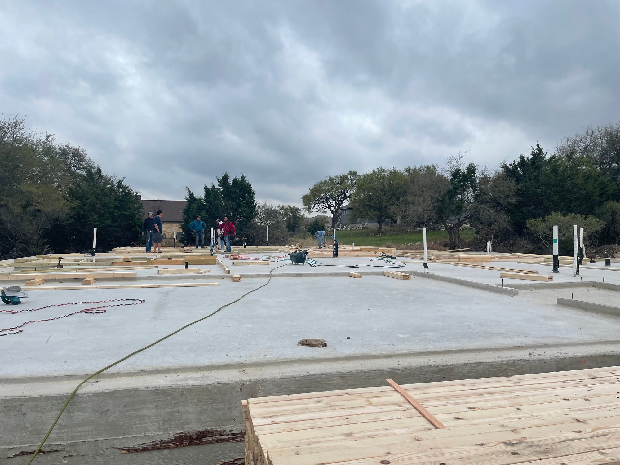 Poured slab with wall plates laid out and a crew working on a Hill Country lot