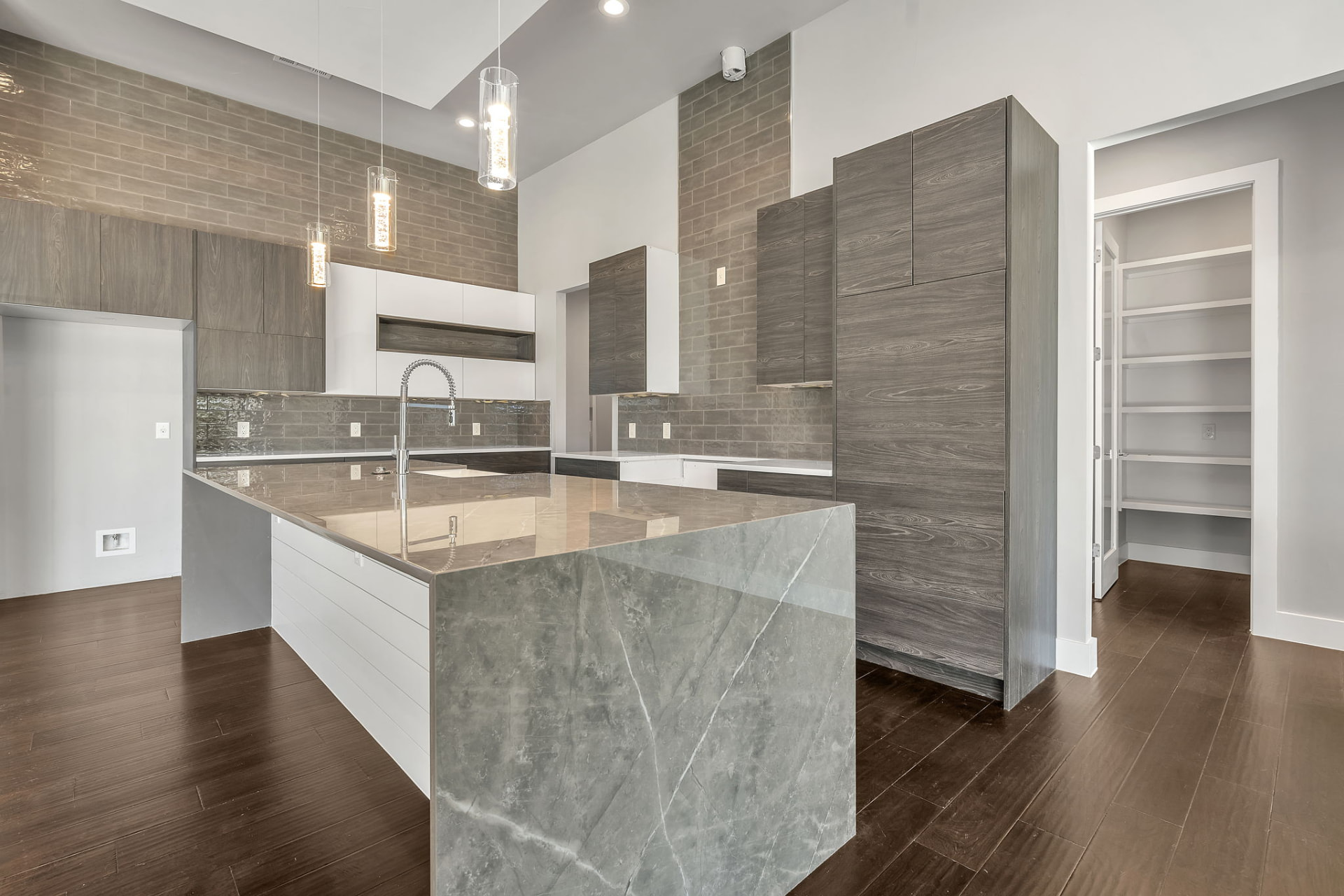 Kitchen with a stone waterfall island, wood grain cabinetry, and walk in pantry