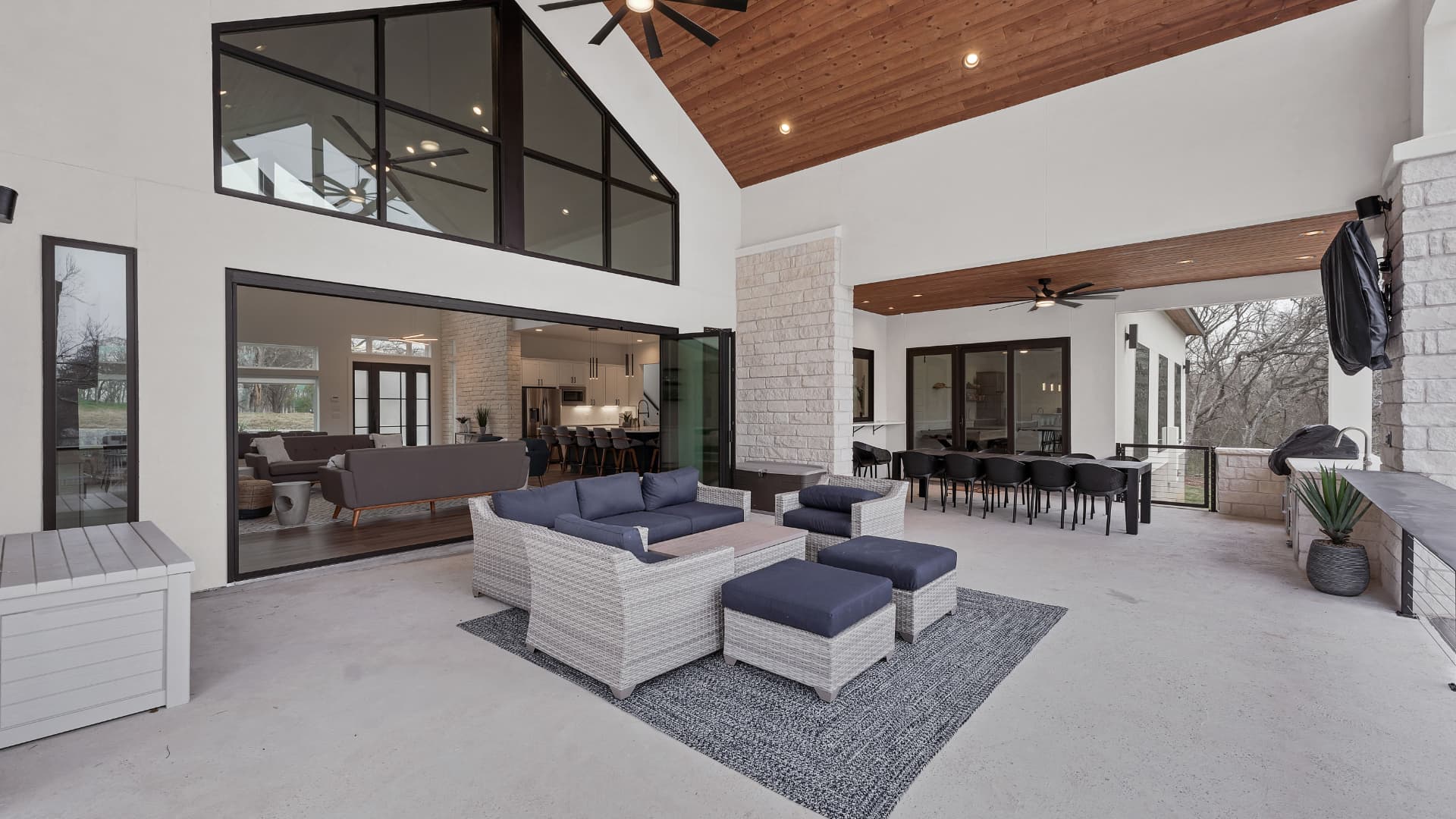 Covered outdoor living area with a stained wood ceiling, grill, and long dining table