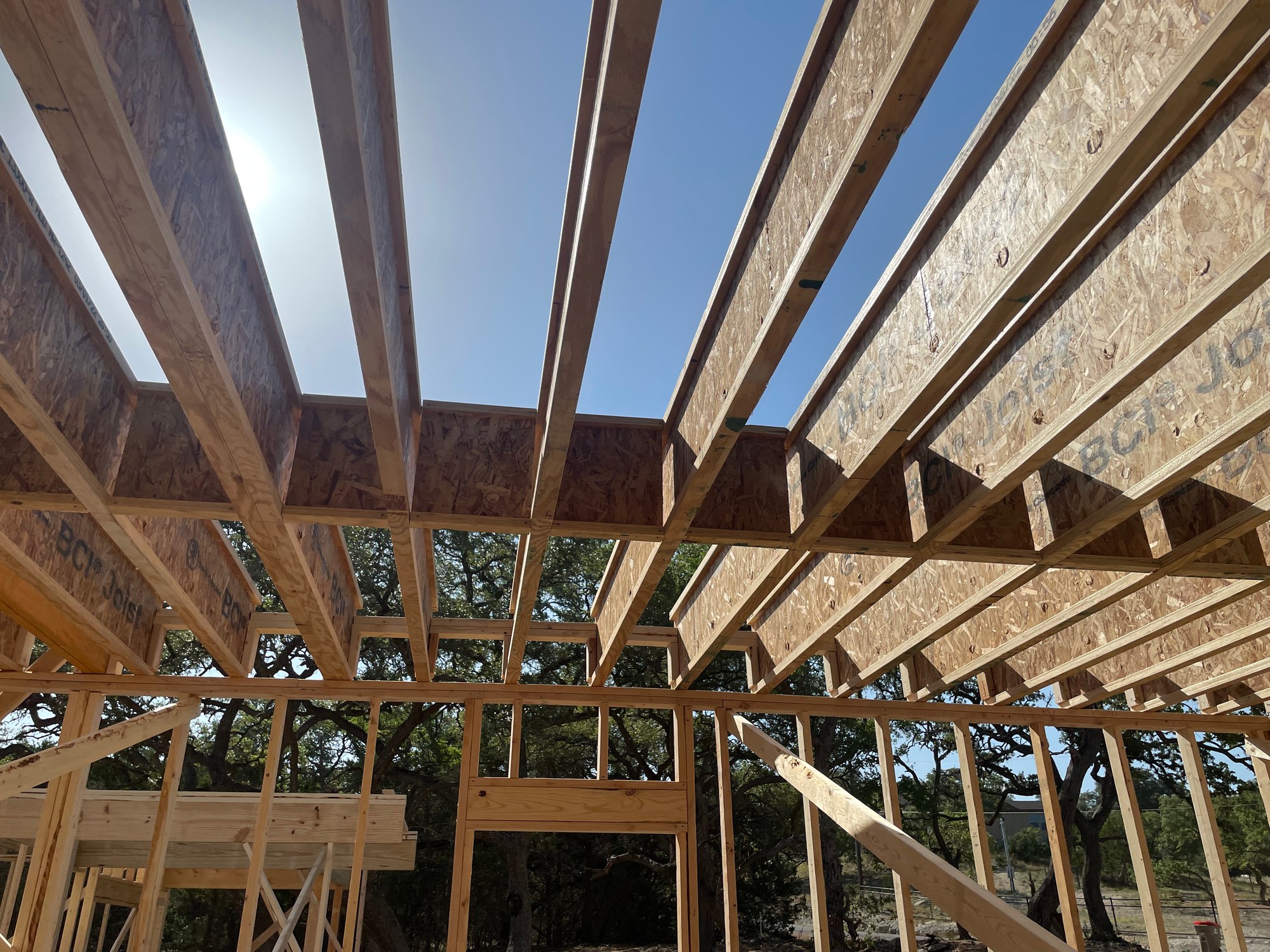 Framed floor system and open wall studs seen from below against a blue sky