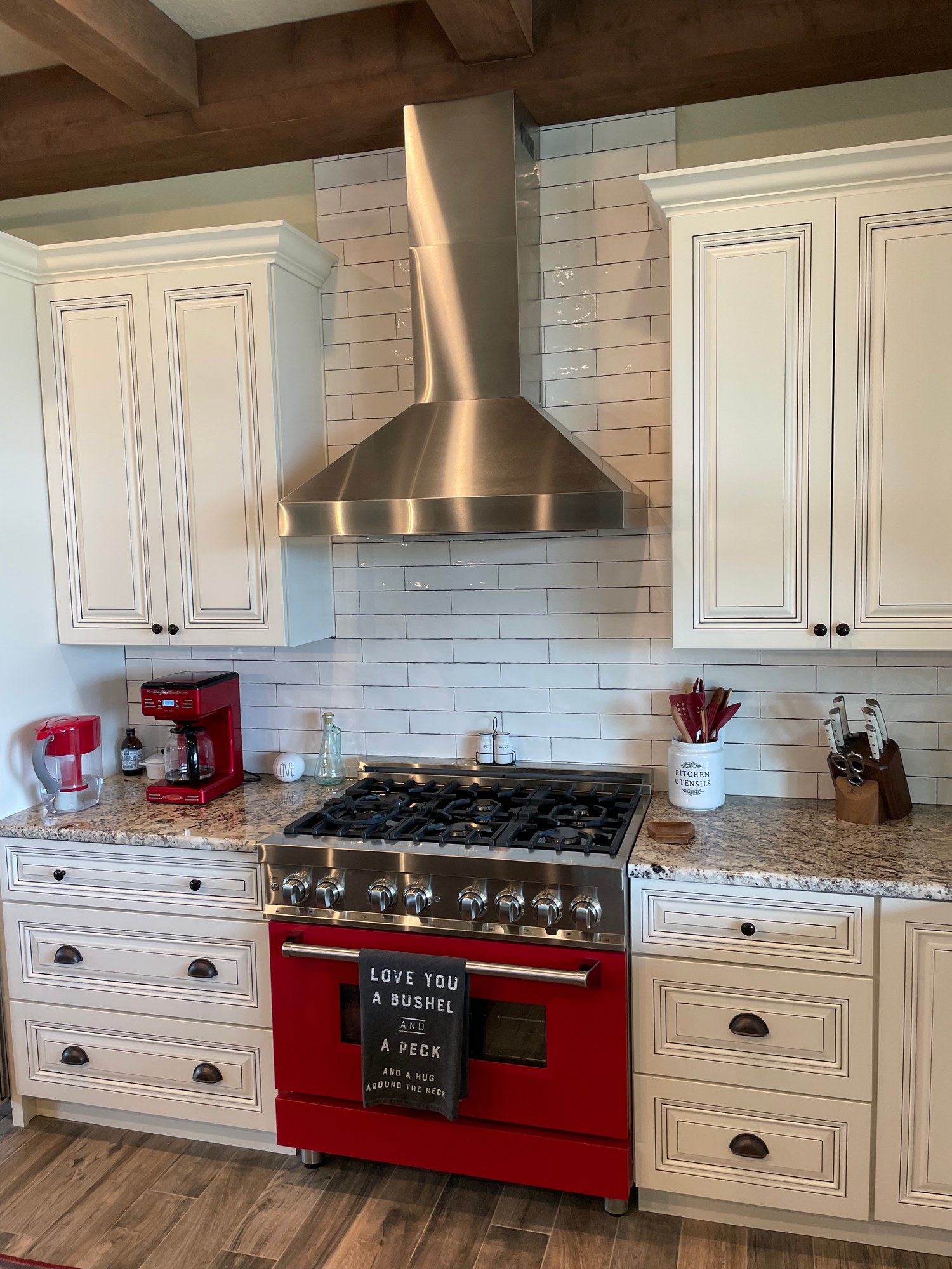 Kitchen range wall with cream cabinetry, subway tile, and a red range
