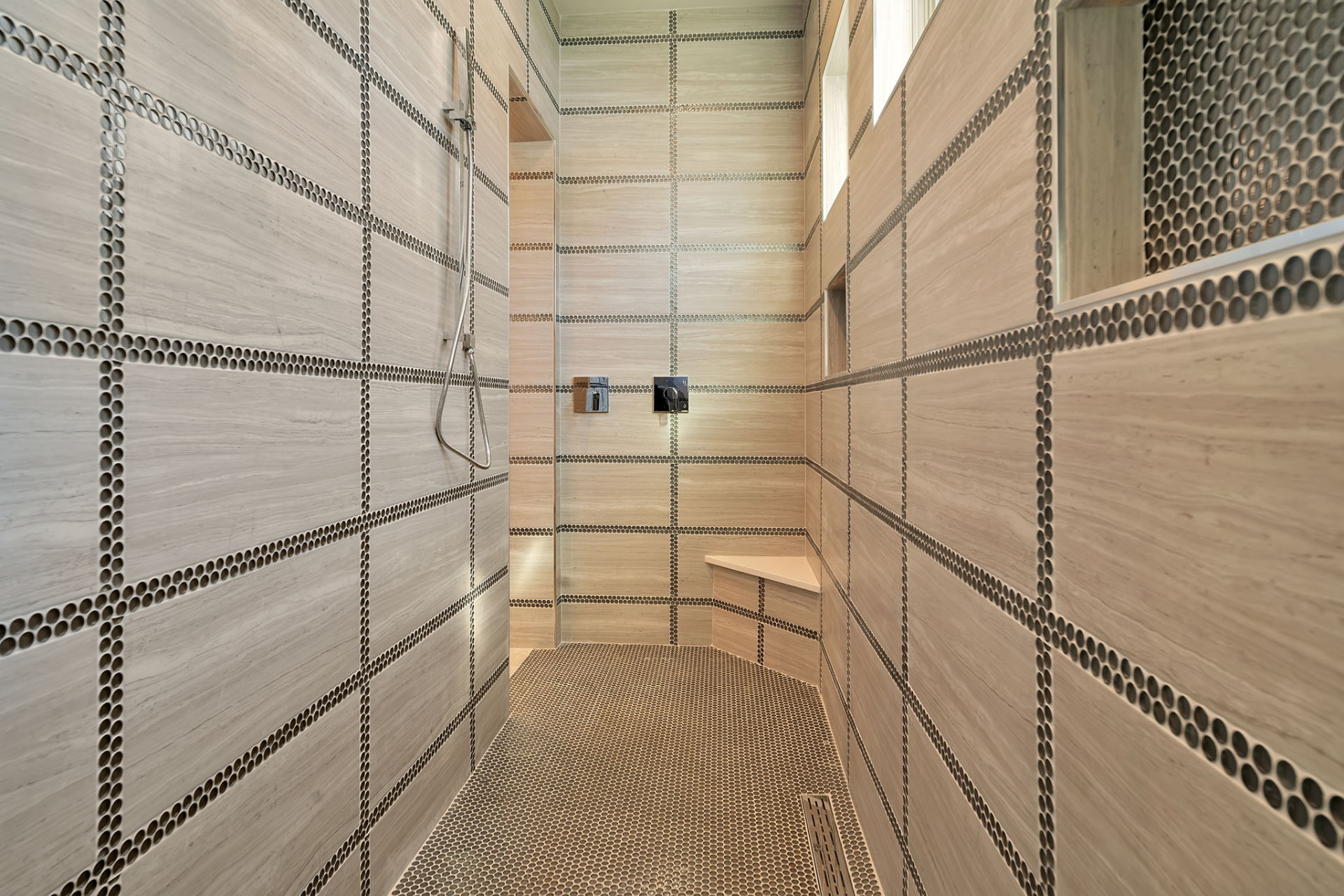 Walk in shower tiled in stone with penny round accent banding