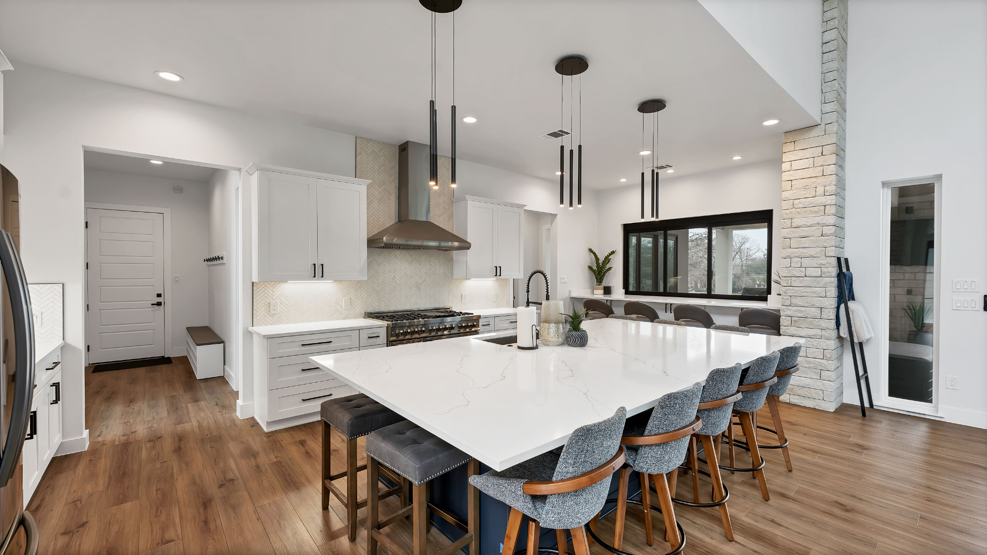 Kitchen with a large quartz island, herringbone backsplash, and range hood