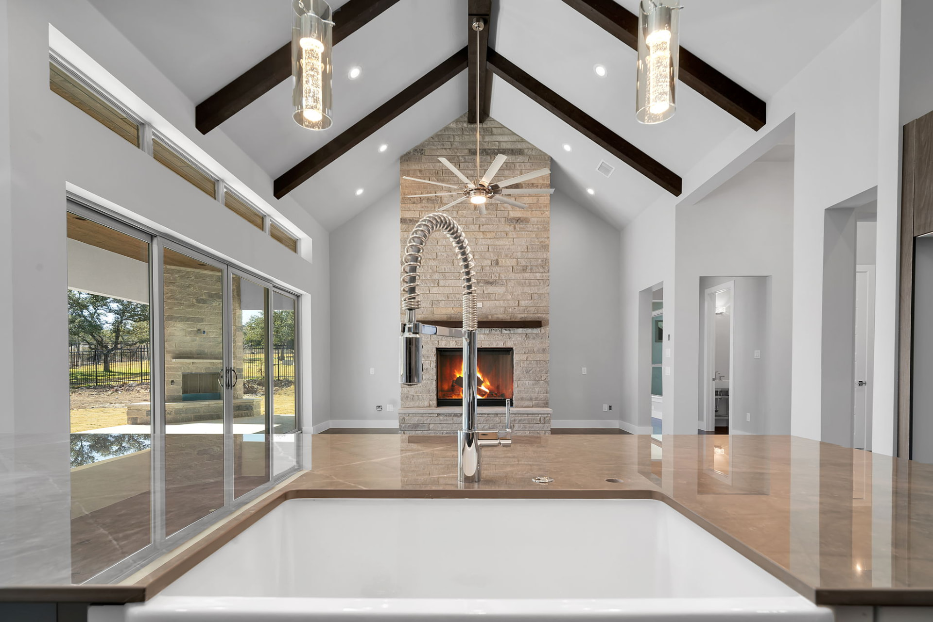 Vaulted living room with exposed beams and a brick fireplace seen from the kitchen sink